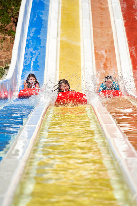 三个孩子在水上乐园玩滑梯。图片素材