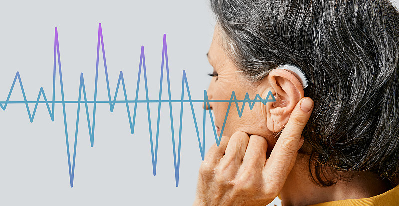 助听器。老年妇女戴着耳背助听器，以声波模式在前景，概念耳聋治疗图片下载