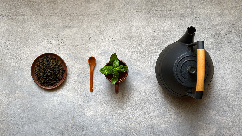 红茶，茶壶和带有薄荷叶的茶杯，在灰色背景上的宽顶视图图片下载