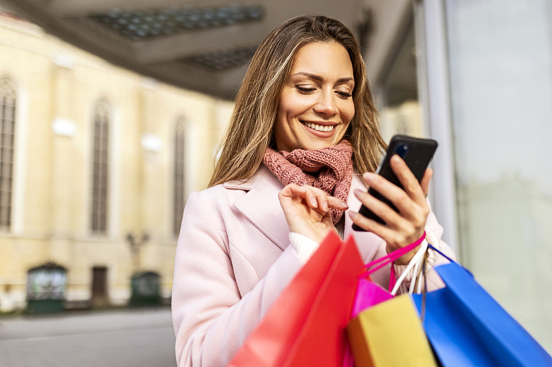 带着购物袋的微笑女人用智能手机发短信图片下载