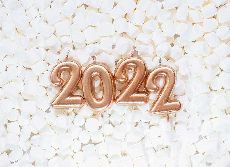 2021年新年快乐。白色棉花糖背景上的金色蜡烛制作的2022年数字。图片下载