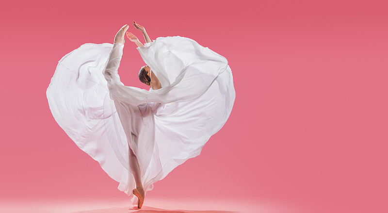 苗条优雅的芭蕾舞女演员在足尖鞋波浪长白色裙子显示一个心形的粉红色背景图片下载