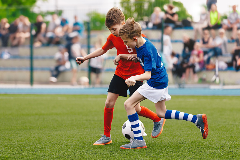 两个孩子在草地上踢足球。快乐的学校男孩踢球在锦标赛比赛。蓝色和红色足球队的孩子们图片下载