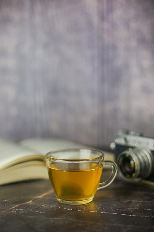 酿造的草本绿茶在透明杯附近打开的书和老式相机在黑暗的背景图片下载