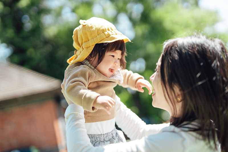 年轻的亚洲母亲在公园里一起消磨时光，把她蹒跚学步的女儿抱到空中图片下载
