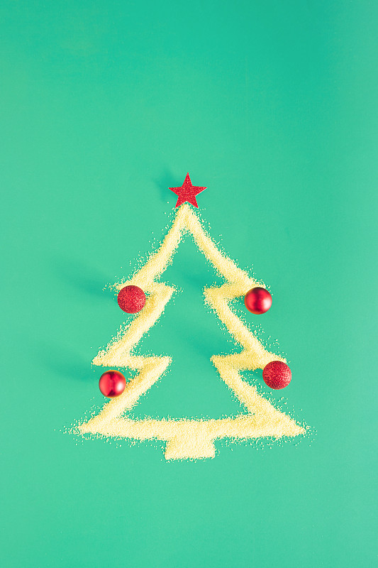 节日安排与圣诞树的形状由黄沙和红色的装饰品在绿色的背景。简约的新年美学与复制空间。创意平面铺设视觉。图片下载