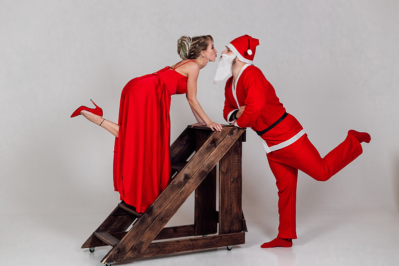 圣诞快乐。在白色背景上，一对穿着红色衣服的年轻雪少女和圣诞老人互动玩耍。现在图片下载