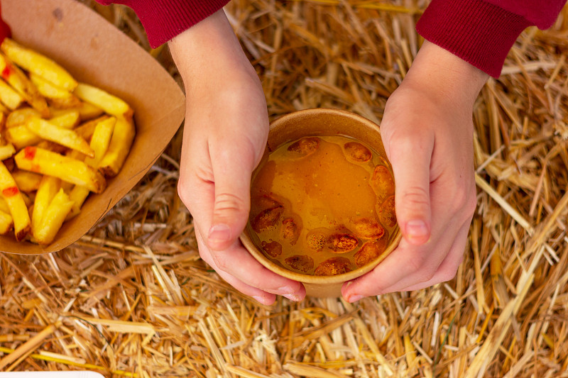 手端着一杯南瓜汤，旁边是放着干草的桌子上的薯片。农民节日上的传统乡村食物。图片下载