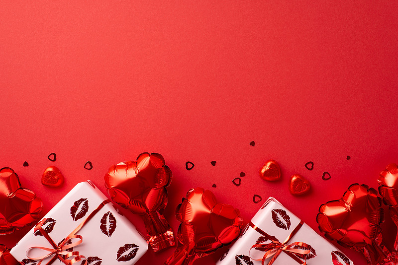 情人节的概念。顶部视图照片心形气球礼盒包装与亲吻嘴唇图案巧克力糖果和纸屑孤立的红色背景与复制空间摄影图片下载
