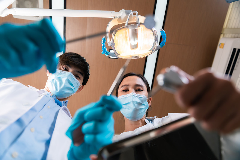 亚洲女牙医调整手术光线从上方看病人。图片下载