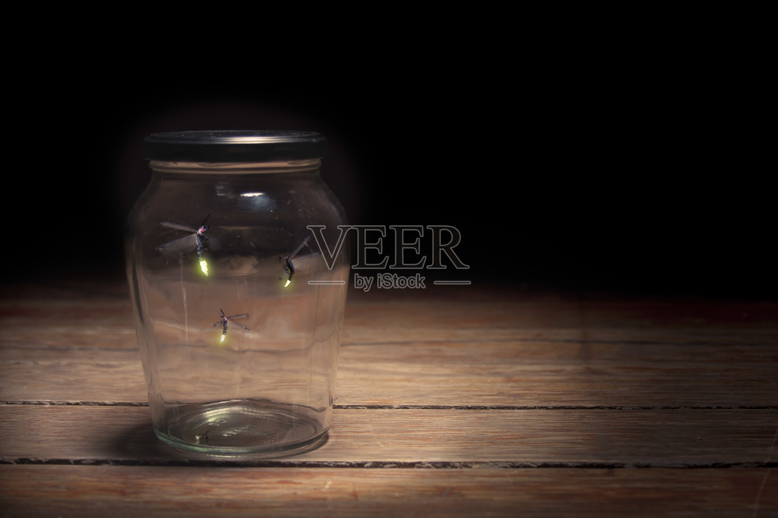 三只萤火虫被困在木桌上的一个玻璃罐子里照片摄影图片