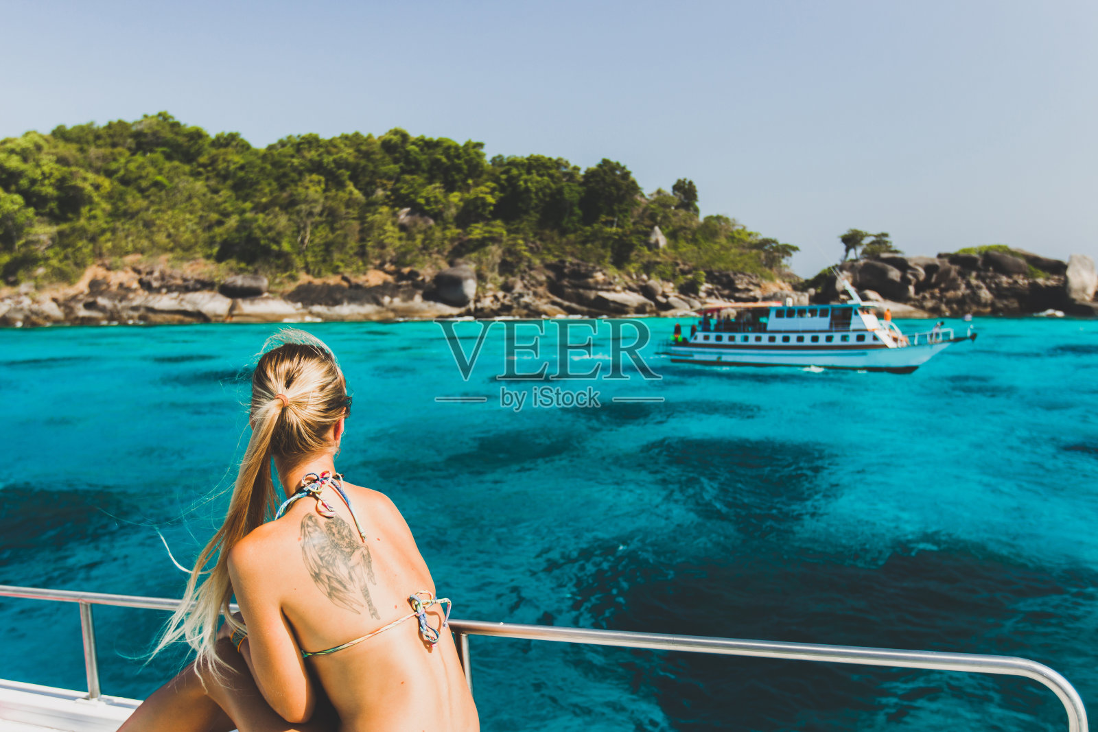 背上有纹身的金发女子在豪华游艇上放松，看到天堂般的热带岛屿和绿松石般的海水照片摄影图片