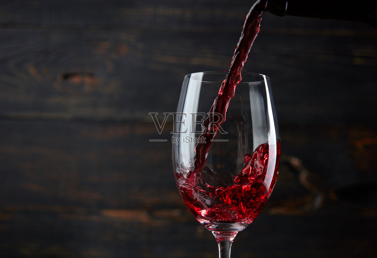在深色的木质背景下，将红酒倒入玻璃杯中照片摄影图片