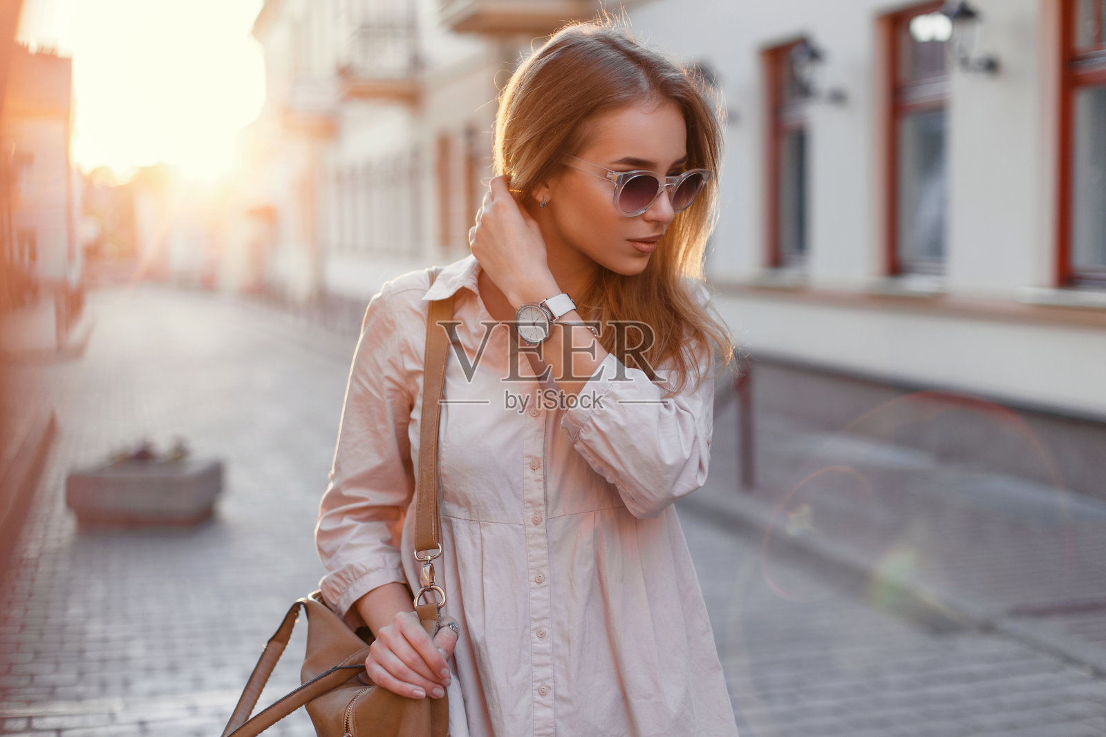 美丽的女孩戴着时尚的太阳镜和包在日落。照片摄影图片
