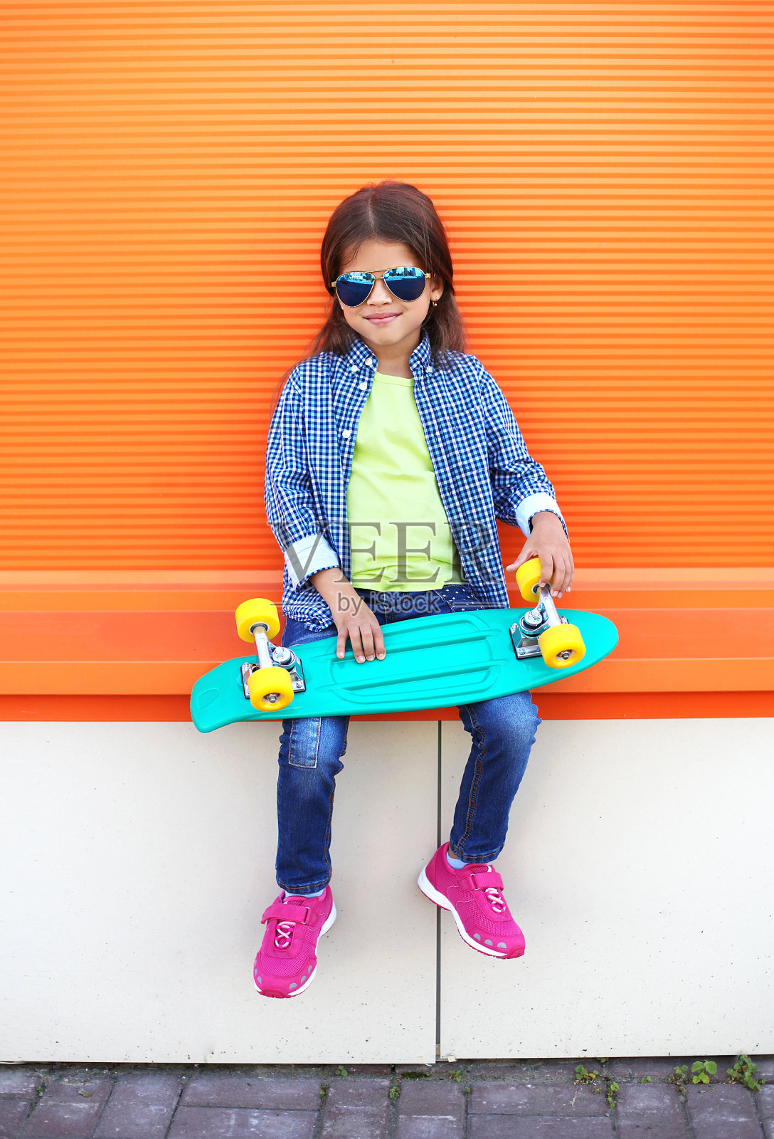 穿着滑板的时尚孩子戴着太阳镜在橙色的背景照片摄影图片