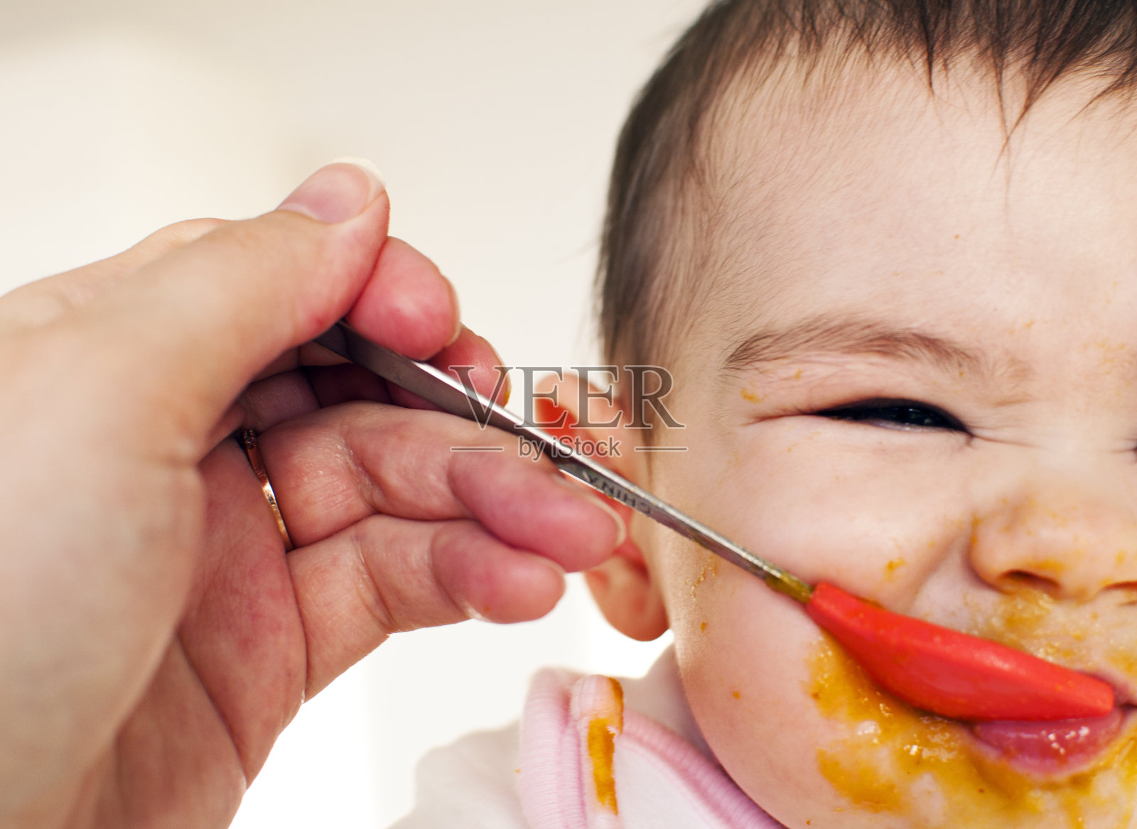 婴儿被人用汤匙喂着，脸上露出厌恶的表情照片摄影图片