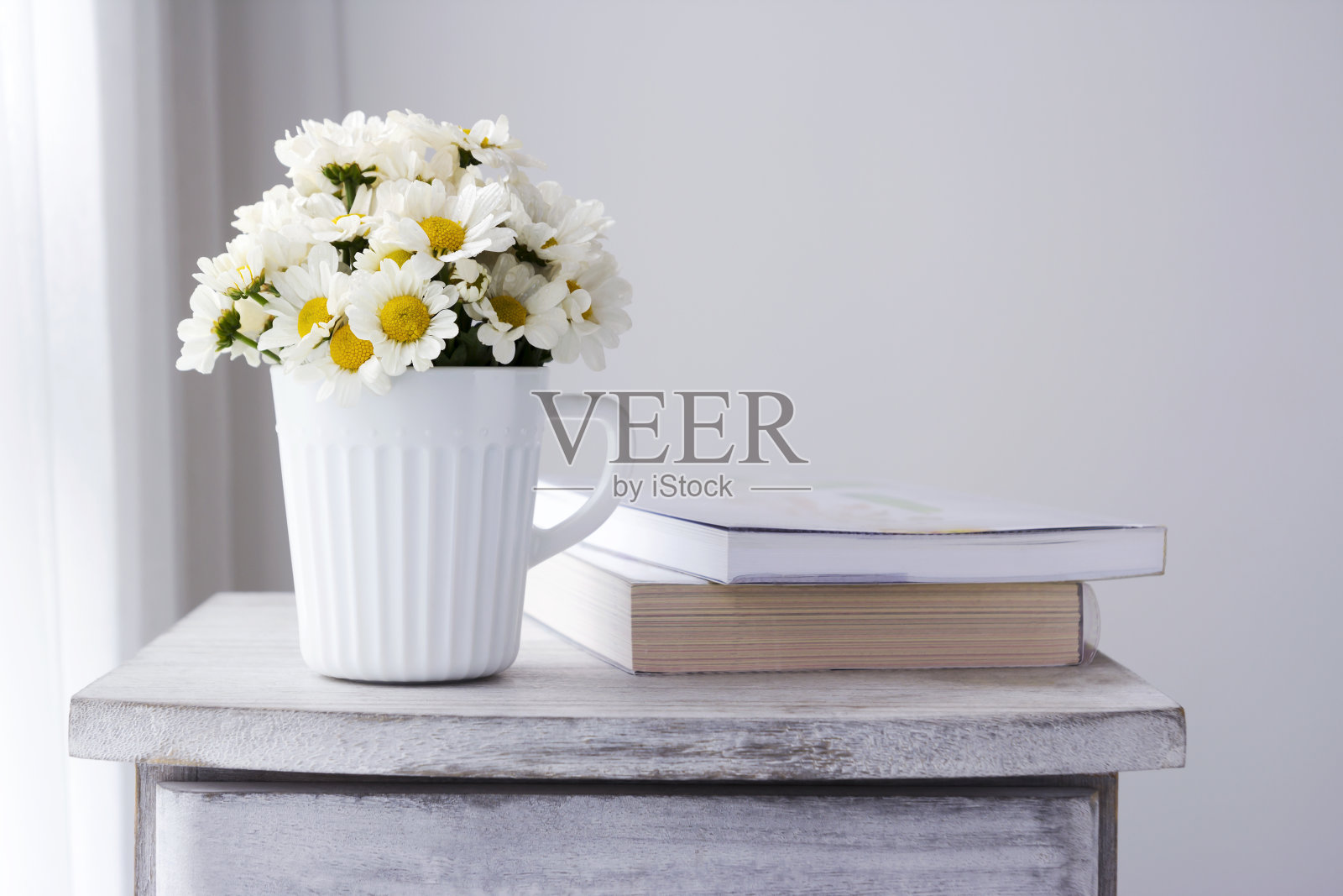 新鲜的雏菊花装在白色的杯子里，放在木柜上照片摄影图片