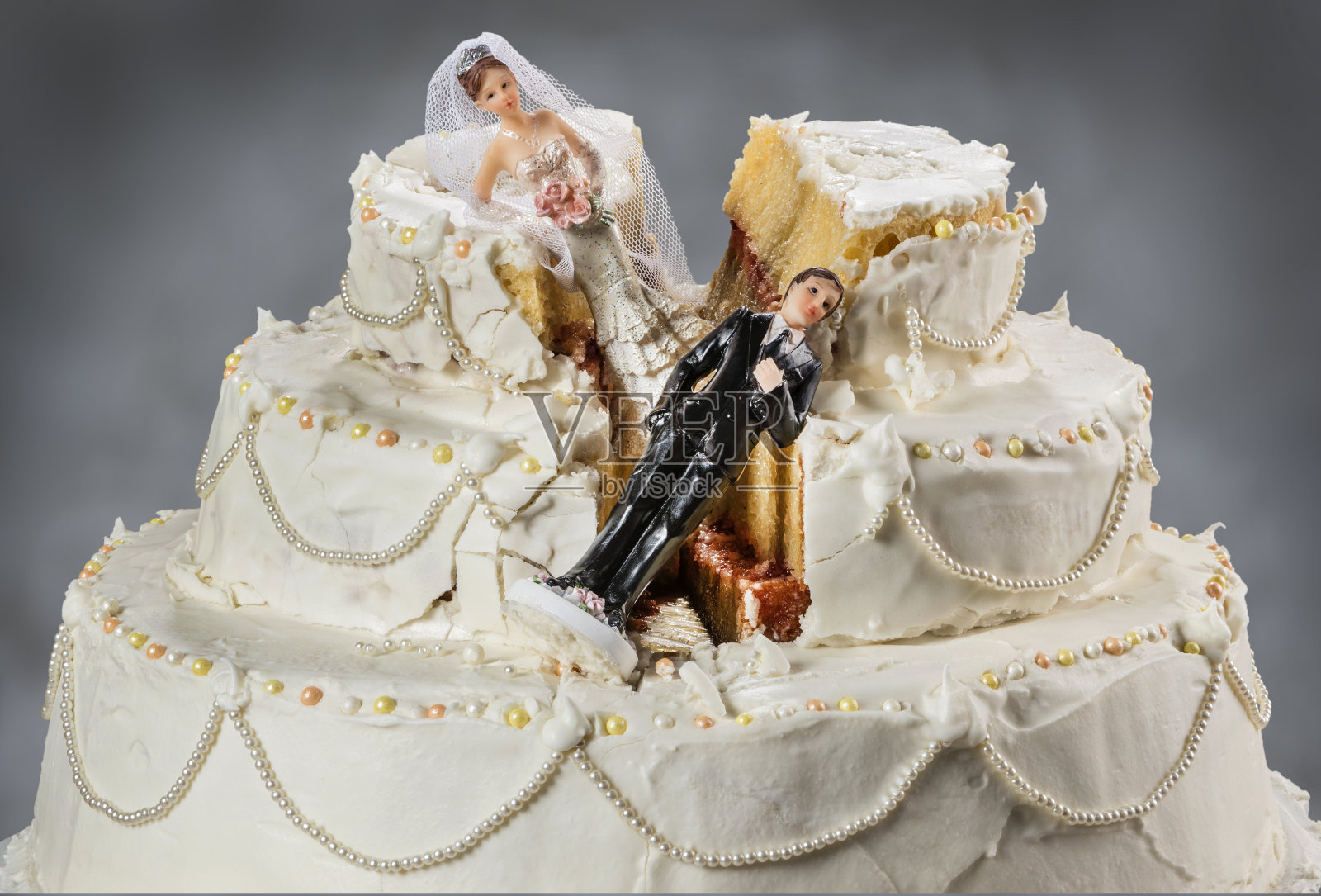 新娘和新郎的小雕像倒在了毁了的婚礼蛋糕上照片摄影图片