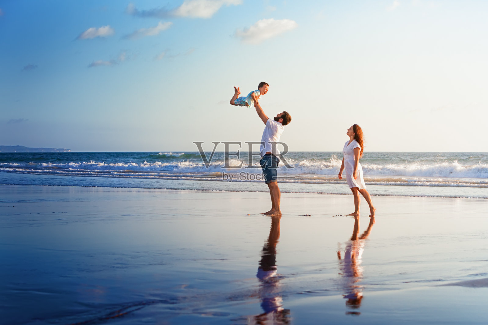 快乐的家庭漫步在日落的海滩上照片摄影图片