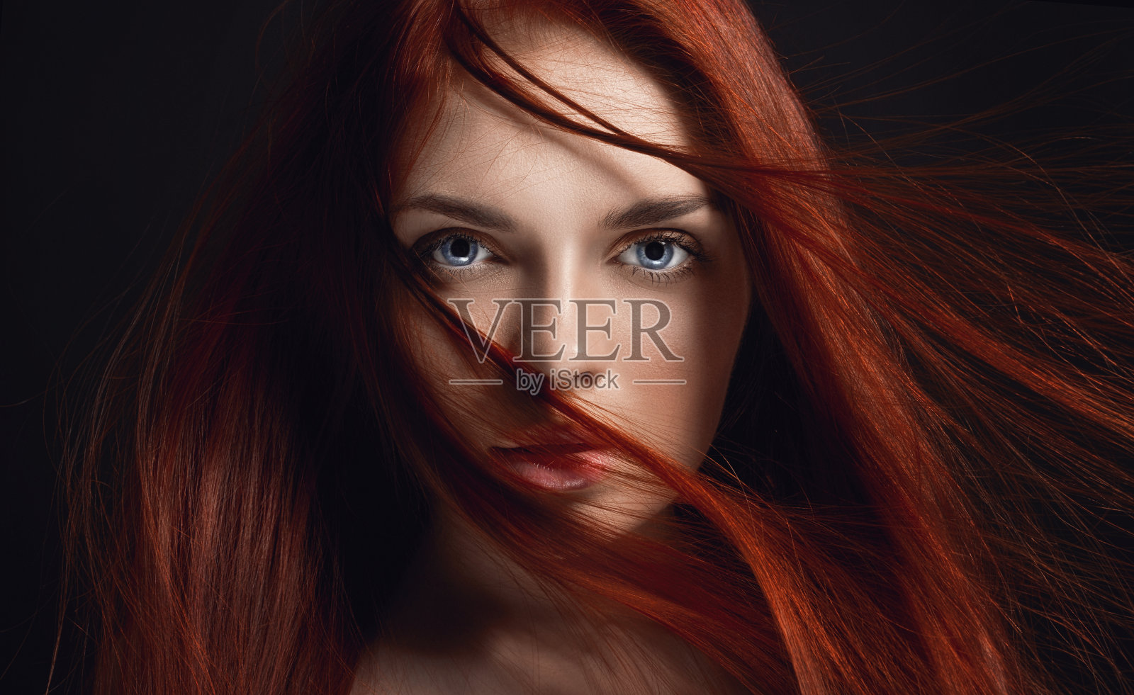 性感漂亮的长头发红发女孩。完美的女人肖像在黑色的背景。漂亮的头发和深邃的眼睛。自然美，清洁皮肤，面部护理和头发。强壮而浓密的头发。花照片摄影图片