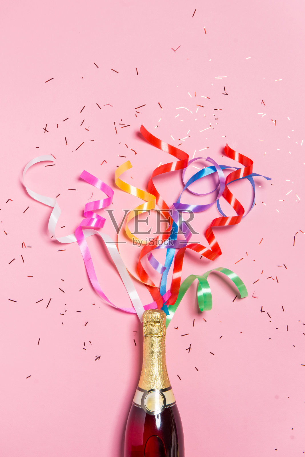 粉红色背景上有彩色派对彩带的香槟酒瓶。照片摄影图片