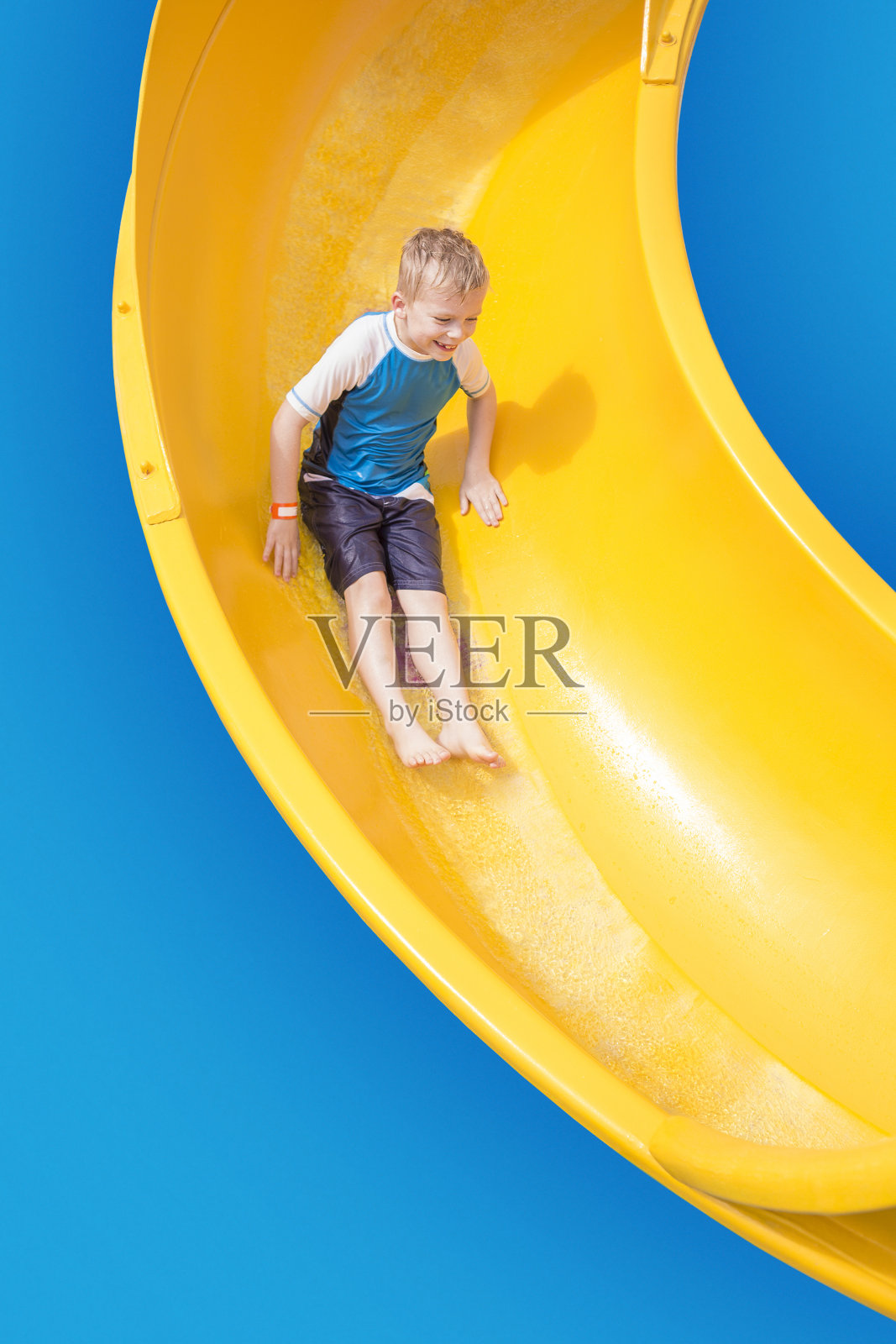 微笑的小男孩骑下黄色的水滑梯照片摄影图片