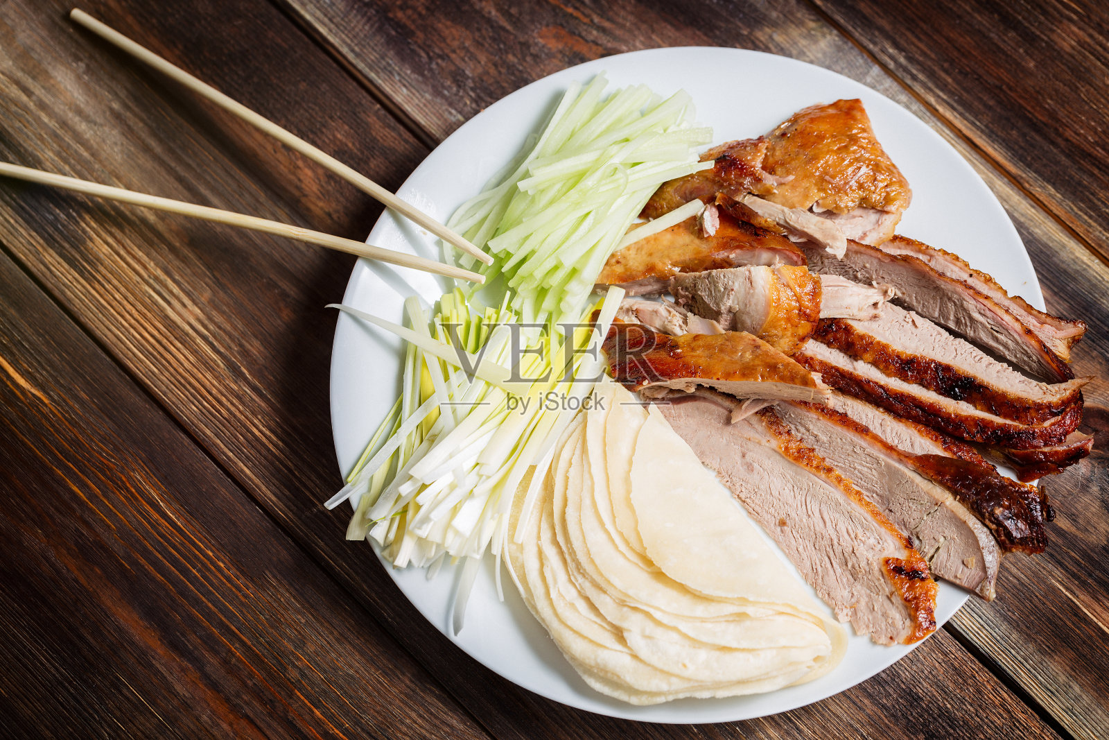北京烤鸭——中国烤鸭配黄瓜片，洋葱，煎饼放在白色盘子里。木制桌子和俯视图照片摄影图片