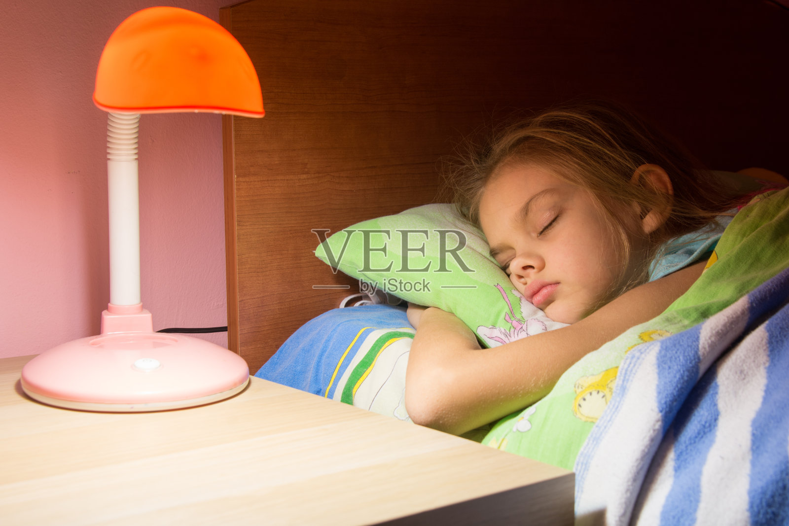 七岁的小女孩睡在床上，台灯就放在旁边的桌子上照片摄影图片