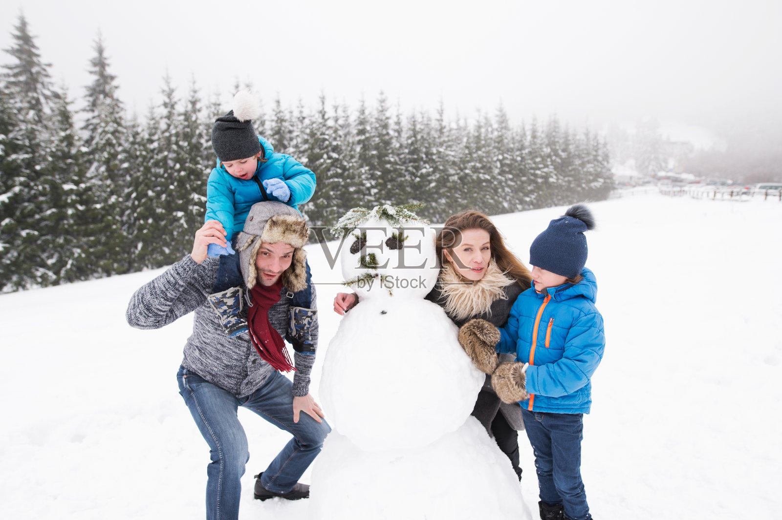 父母和他们的儿子，在雪中玩耍，堆雪人。照片摄影图片