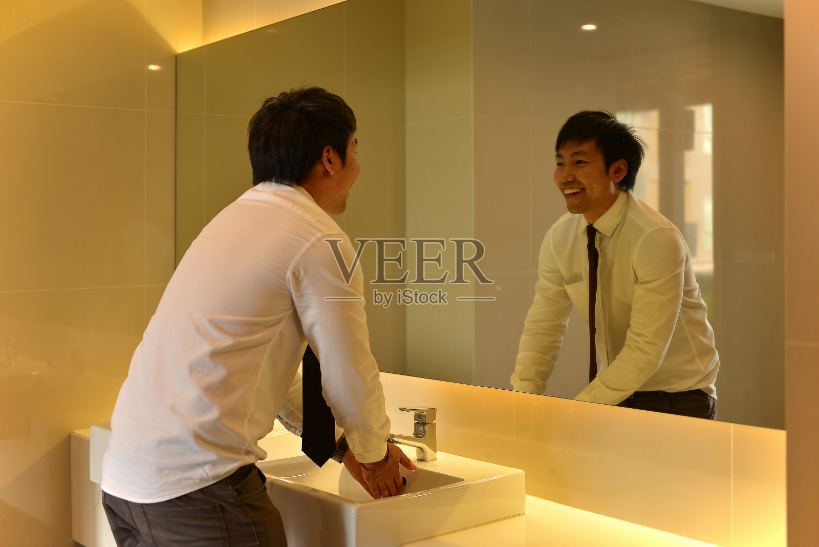 一个亚洲男人在卫生间里洗手，看着豪华卫生间里的人照片摄影图片