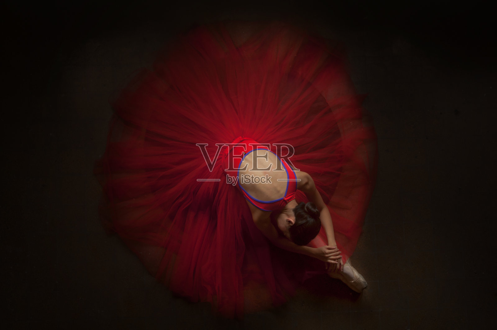 美丽的芭蕾舞女演员躺在她的膝盖上，穿着美丽的红色短裙照片摄影图片