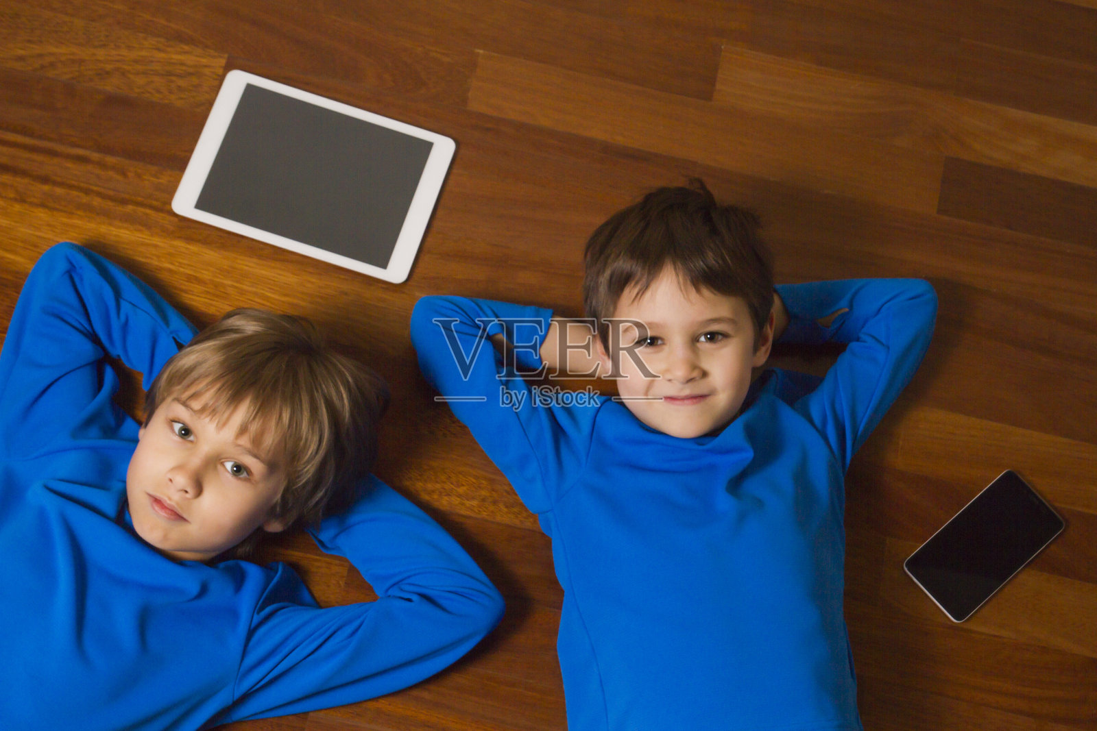 孩子们拿着平板电脑、手机躺在木地板上照片摄影图片
