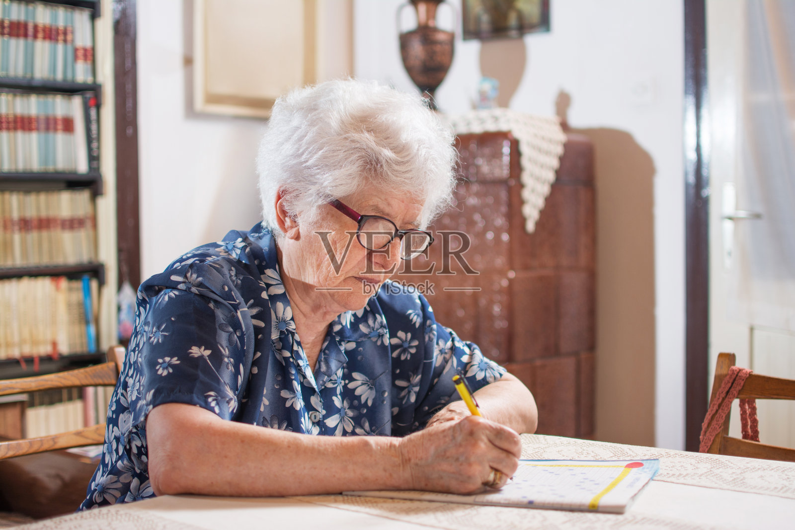 坐在桌旁做填字游戏的老妇人。照片摄影图片