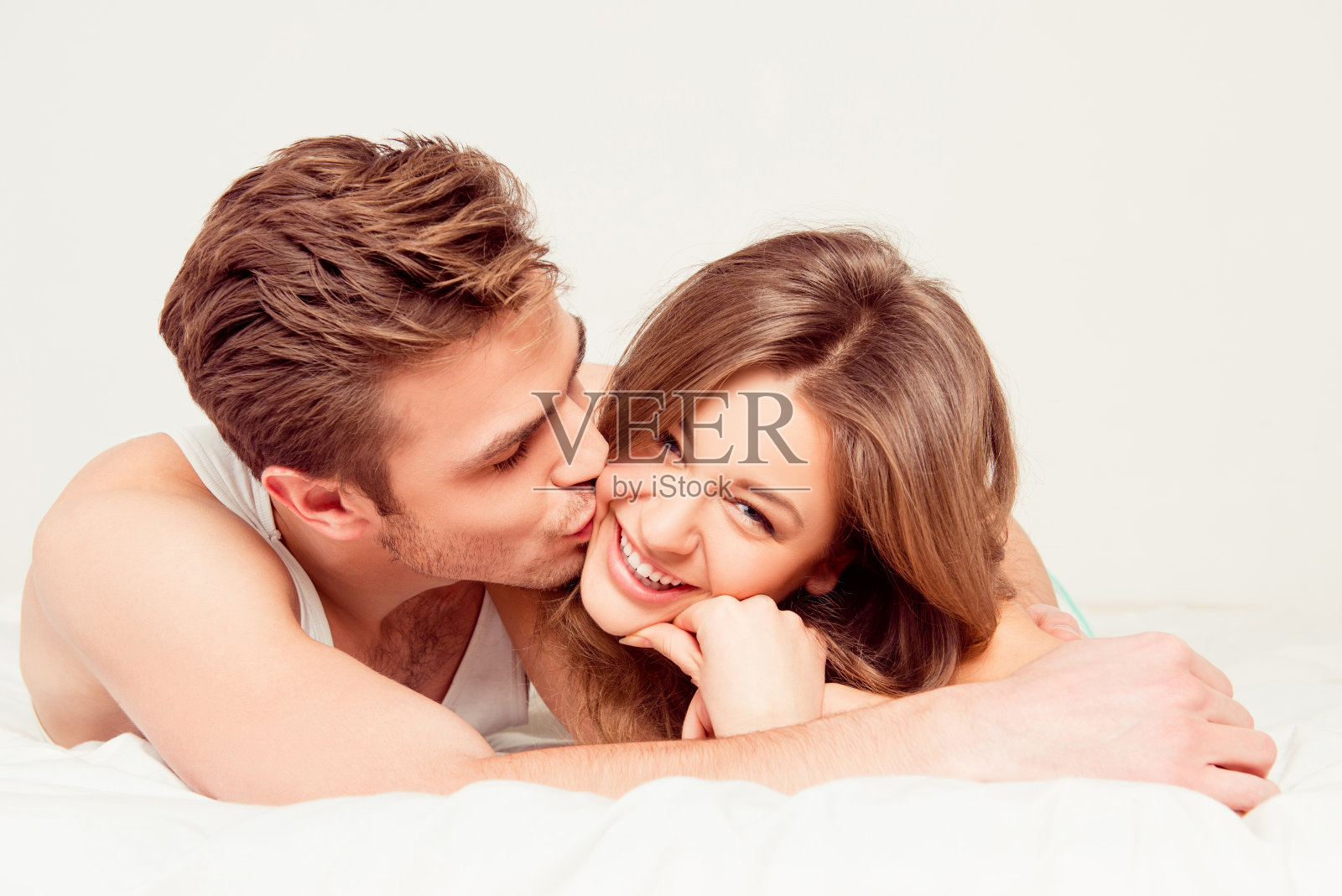 快乐可爱的男人亲吻躺在床上的女朋友照片摄影图片