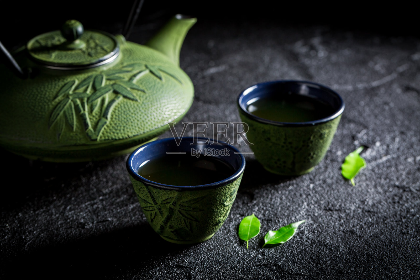 绿茶，茶壶和茶杯放在黑岩上照片摄影图片