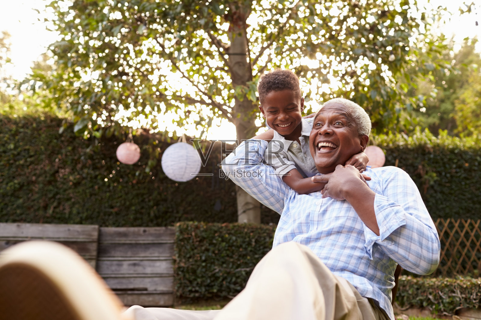 年轻的黑人男孩拥抱祖父坐在花园里照片摄影图片