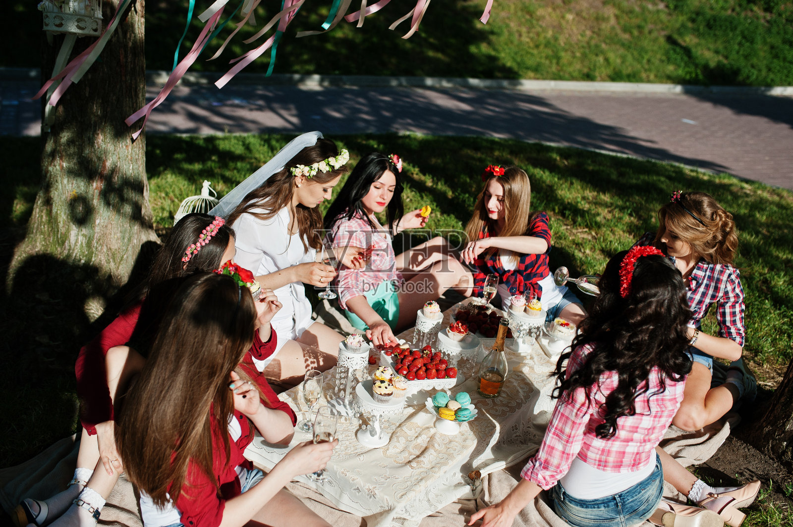 七个快乐性感的女孩坐在野餐桌旁，在单身派对上吃草莓照片摄影图片