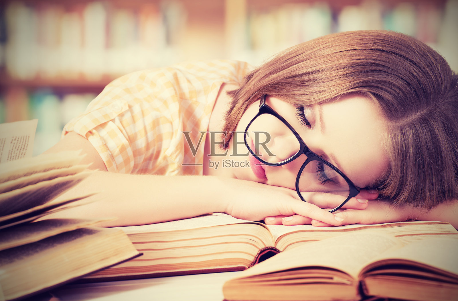 疲惫的戴眼镜的女学生睡在图书馆的书上照片摄影图片