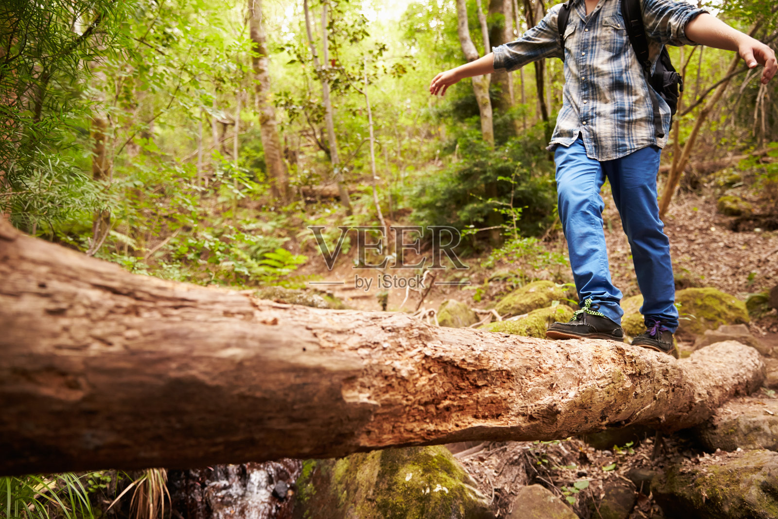 在森林里，男孩在倒下的树上平衡着穿过小溪照片摄影图片
