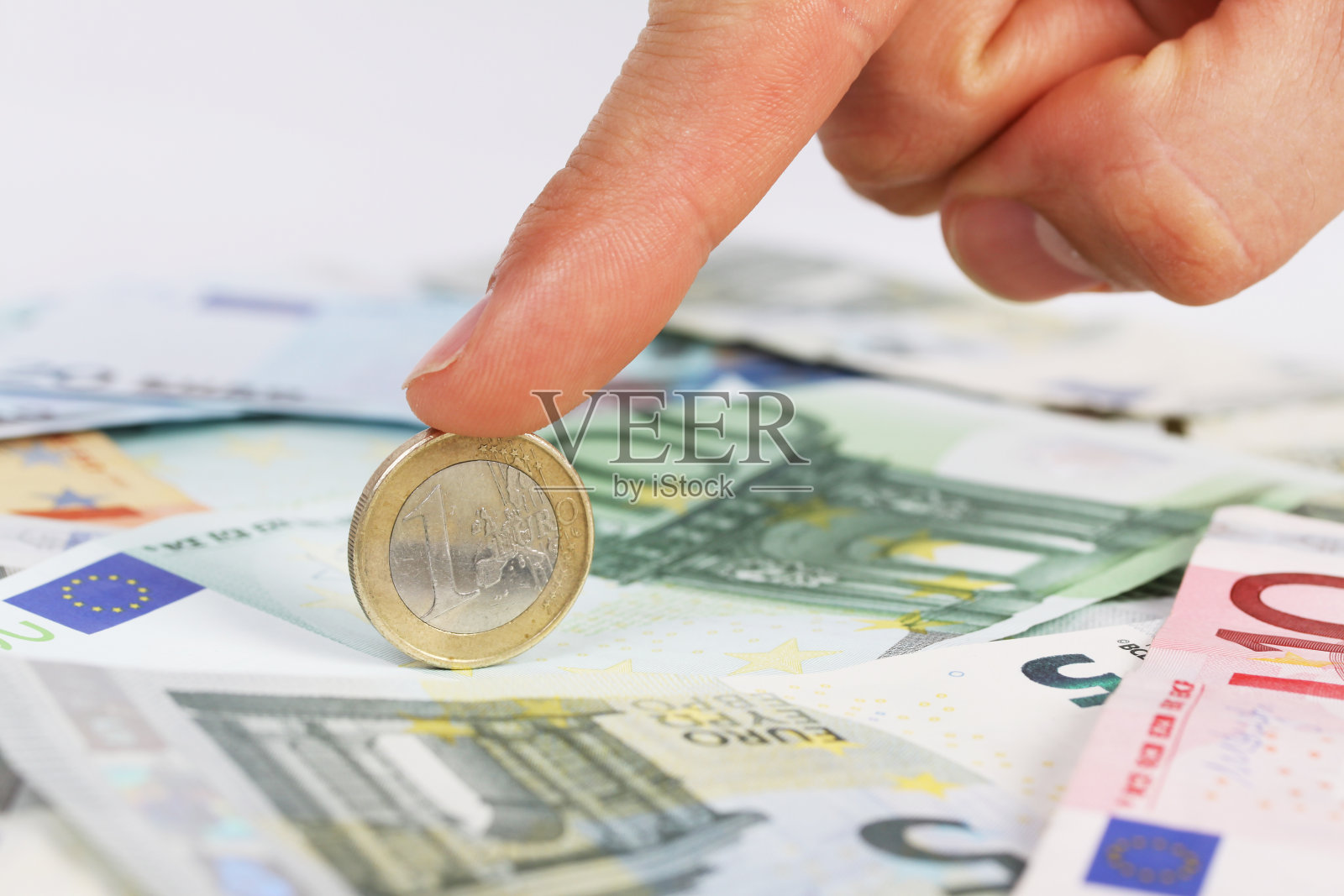 一个男人的手指拿着一枚欧元硬币在欧元纸币上照片摄影图片