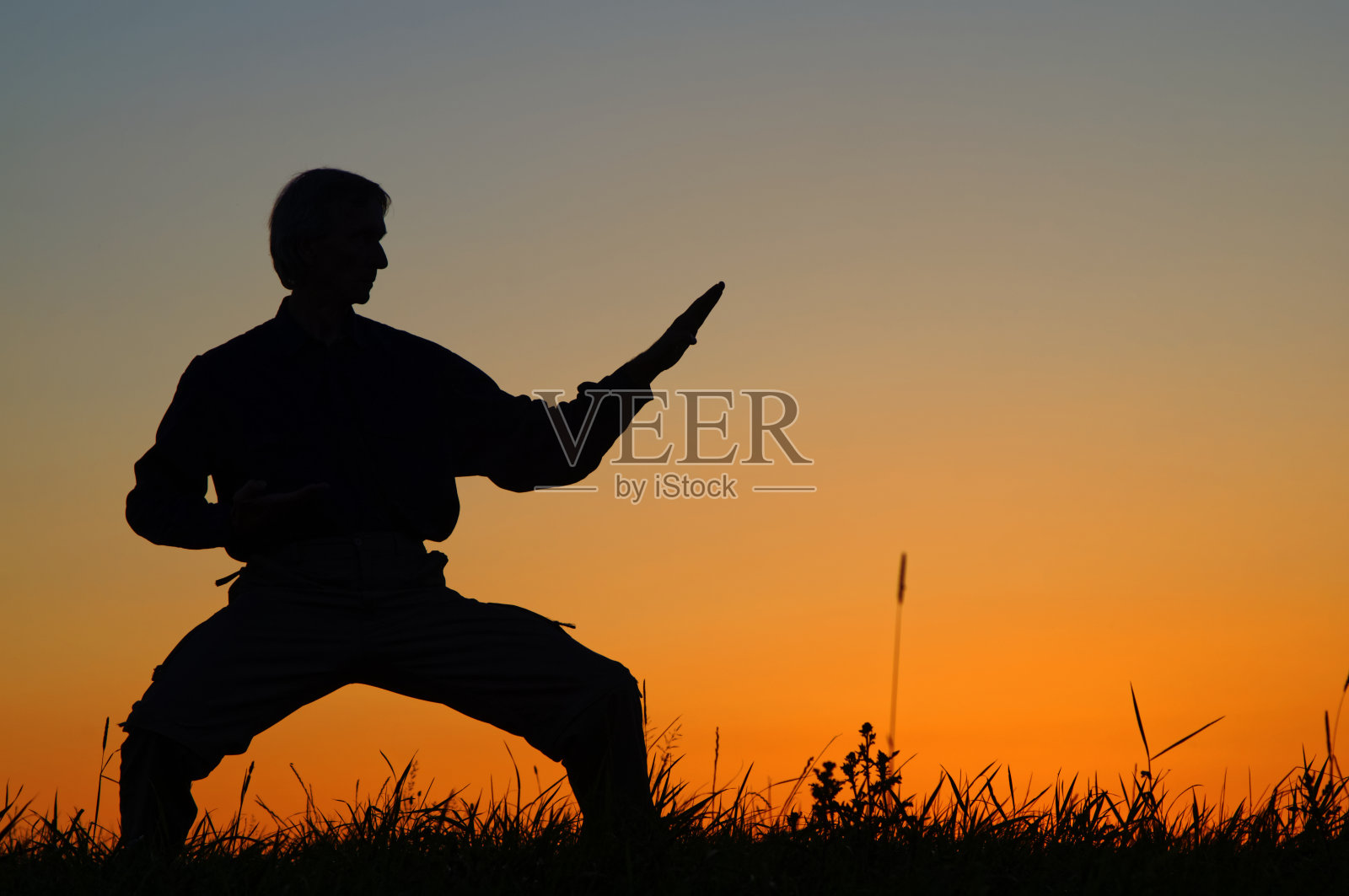 日落后，一名男子在草地上练习空手道。照片摄影图片