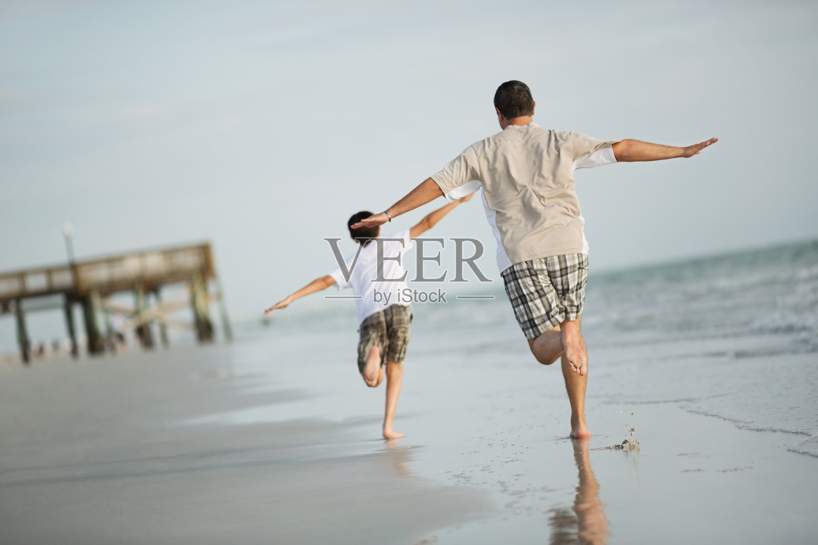 男孩和父亲在沙滩上伸开双臂跑步照片摄影图片