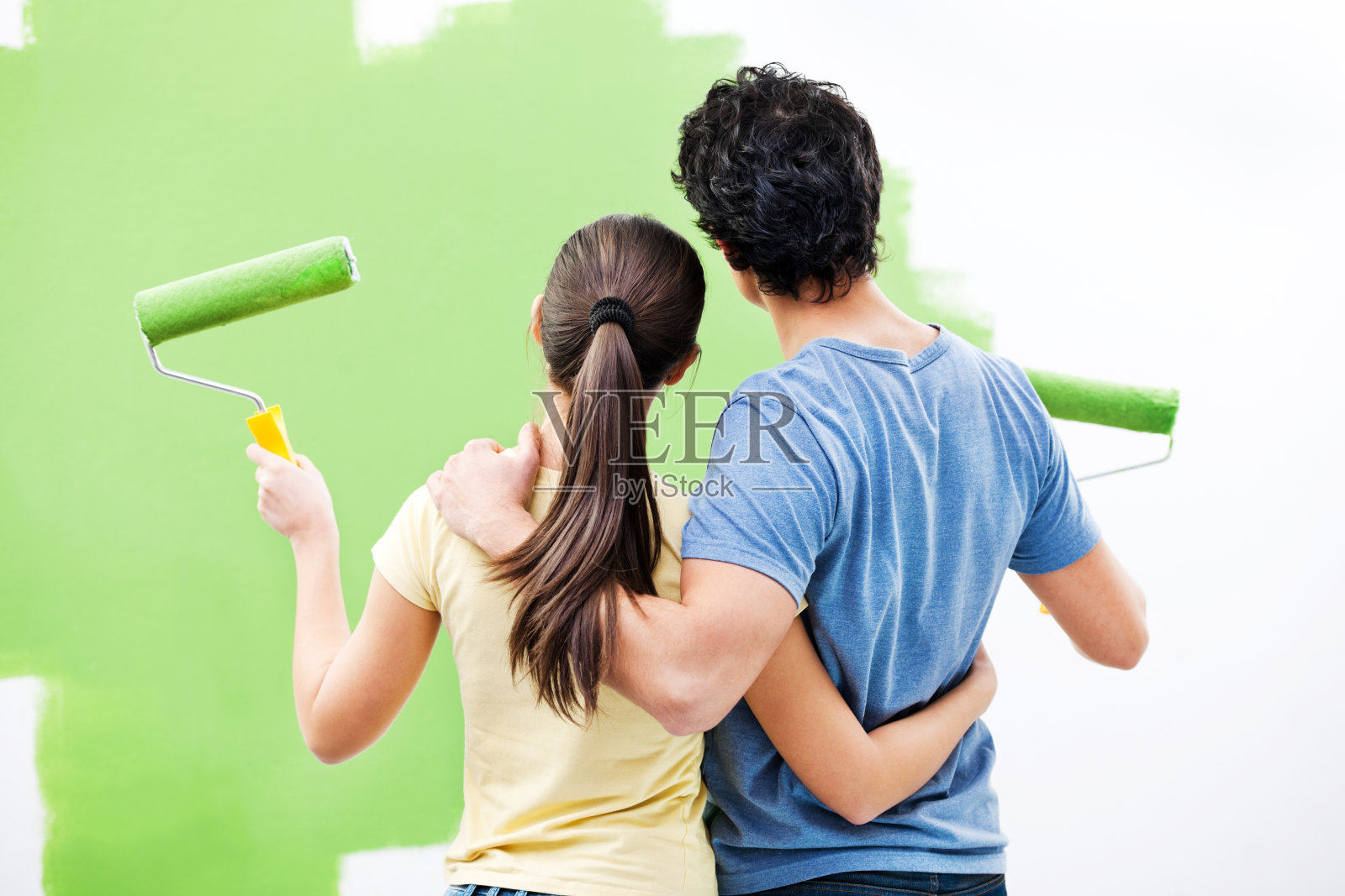 年轻夫妇正在刷墙。照片摄影图片