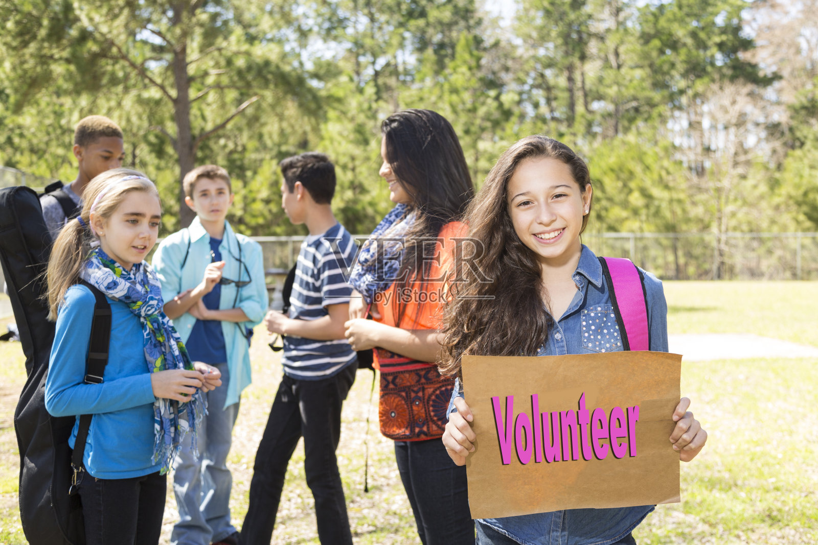 十几岁的拉丁女孩在公园和朋友们举着“志愿者”的牌子。照片摄影图片