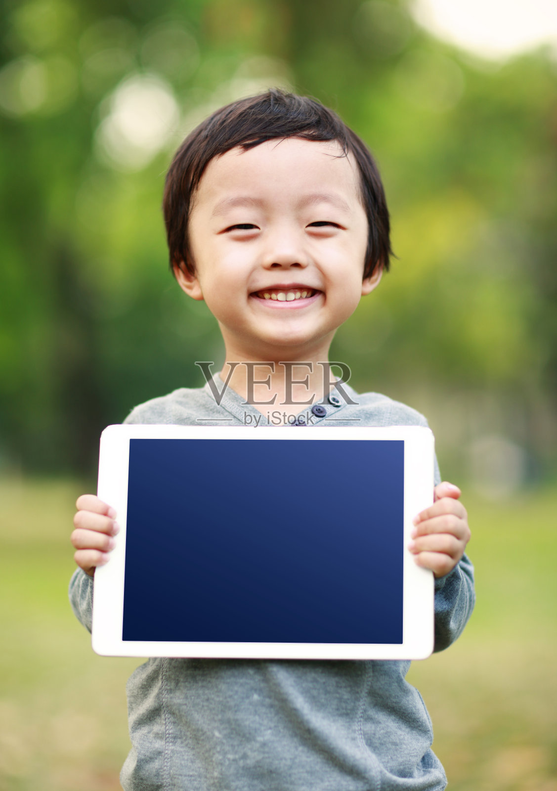 公园里拿着平板电脑的男孩照片摄影图片