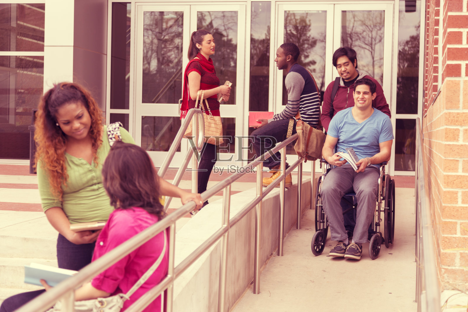 教育:帮助残疾学生下轮椅坡道。大学校园。照片摄影图片
