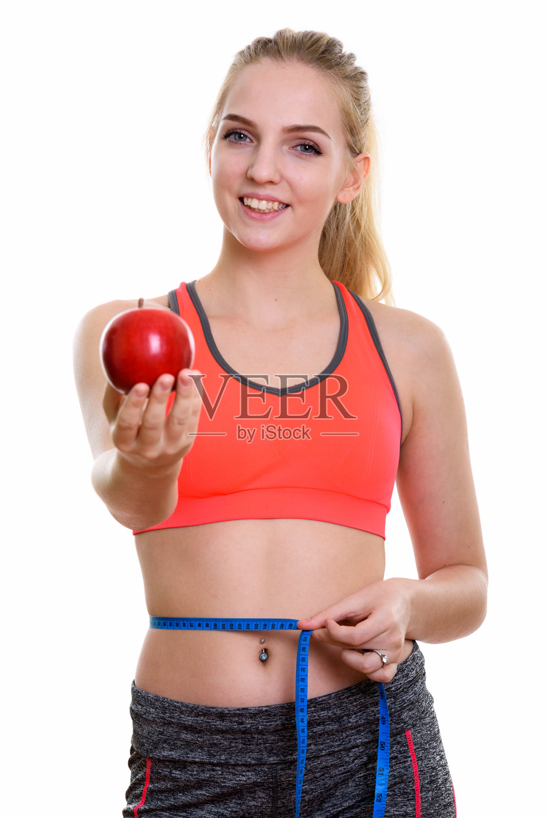 年轻快乐的少女微笑而给红苹果和测量腰围准备健身房照片摄影图片
