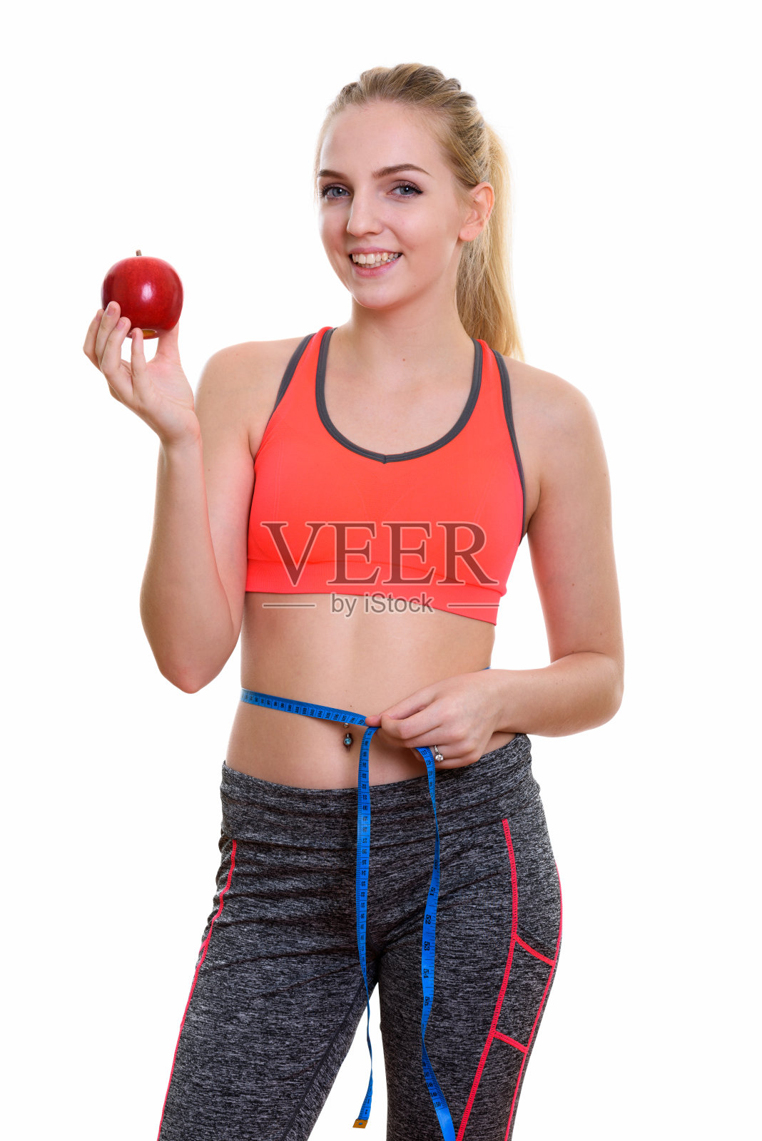 年轻快乐的十几岁的女孩微笑，而持有红苹果和测量腰围准备健身房照片摄影图片