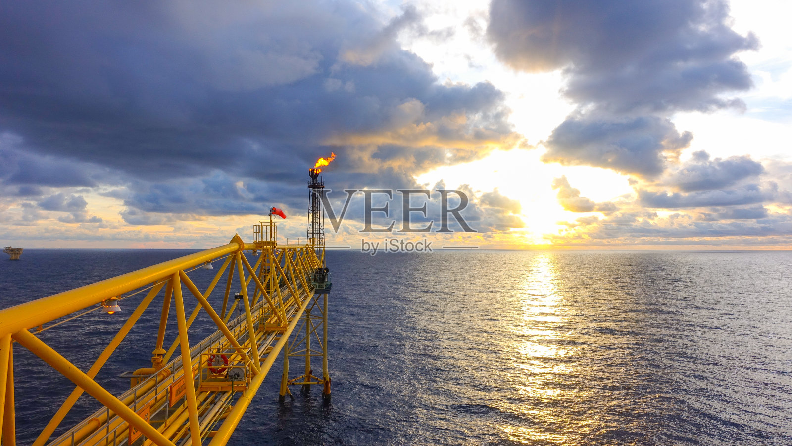 在日出和云层背景下的海上天然气生产平台的火炬桥。照片摄影图片