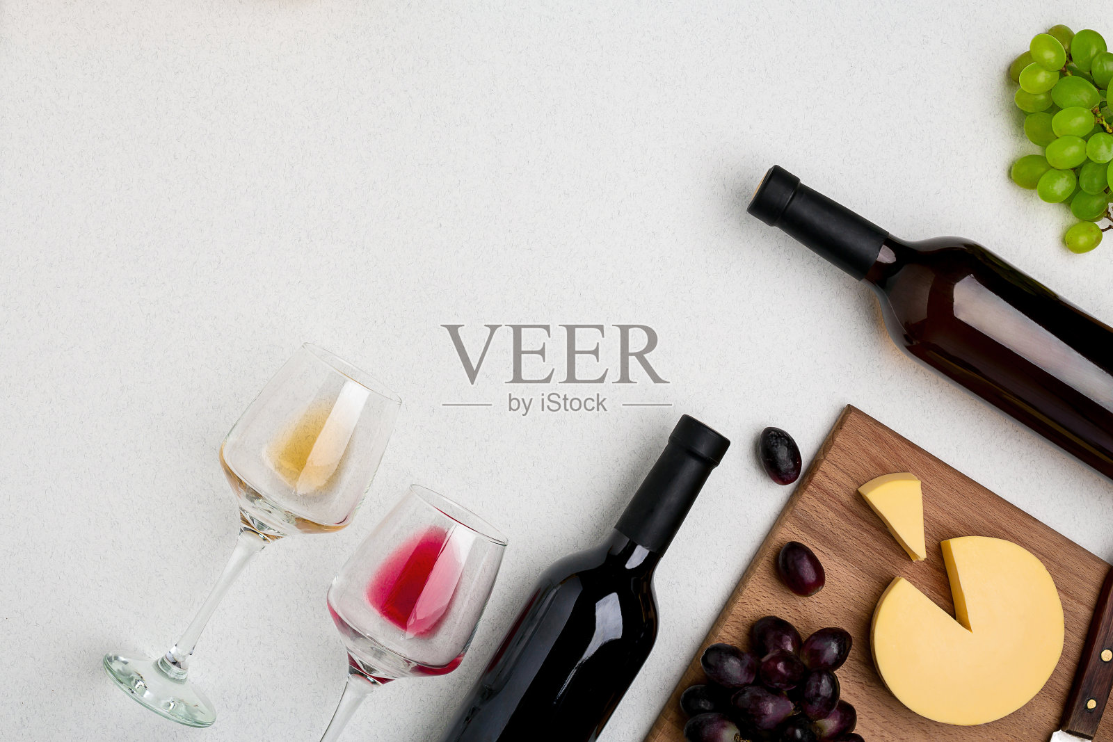 两杯红酒和白酒，一瓶红酒和一瓶白酒，白色背景上的奶酪。从顶部的水平视图照片摄影图片